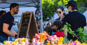 A family shops at the Blacksburg Farmers Market in front of colorful flowers